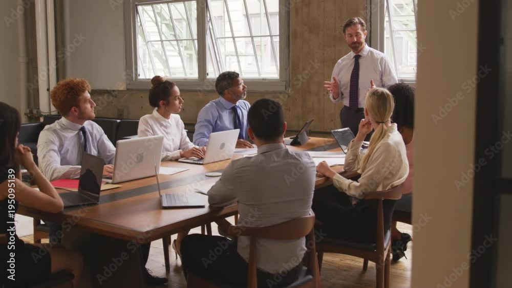 Middle aged businessman leading a meeting, seen from doorway Middle aged businessman leading a meeting, seen from doorway