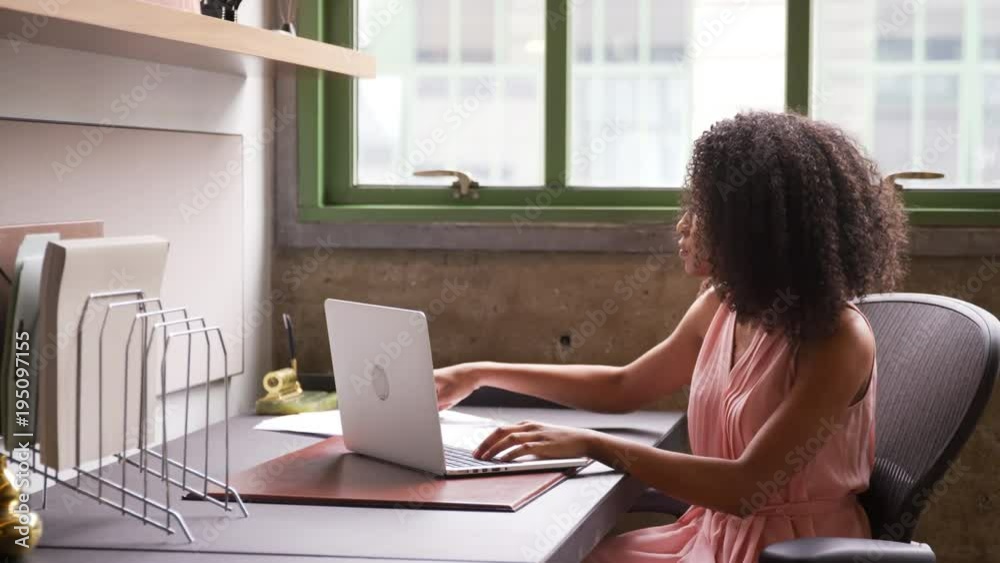 Young black woman working alone with laptop in small office Young black woman working alone with laptop in small office