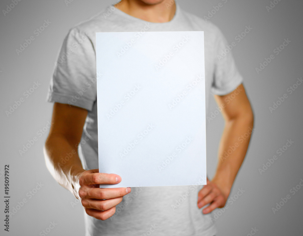 A man in a gray t-shirt keeps a light blue clean blank sheet of A4. Isolated on grey background