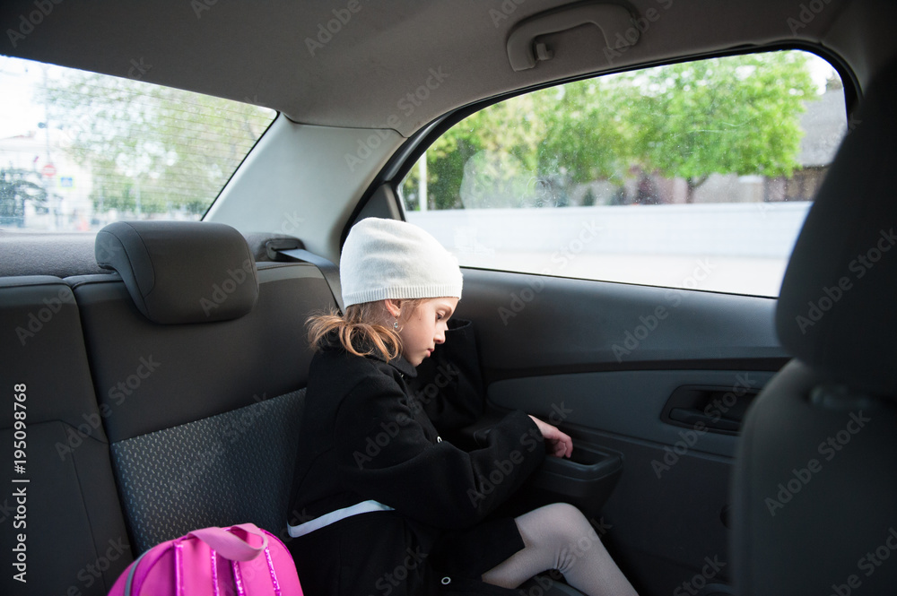 sad little girl in coat and hat sitting with a backpack in the car