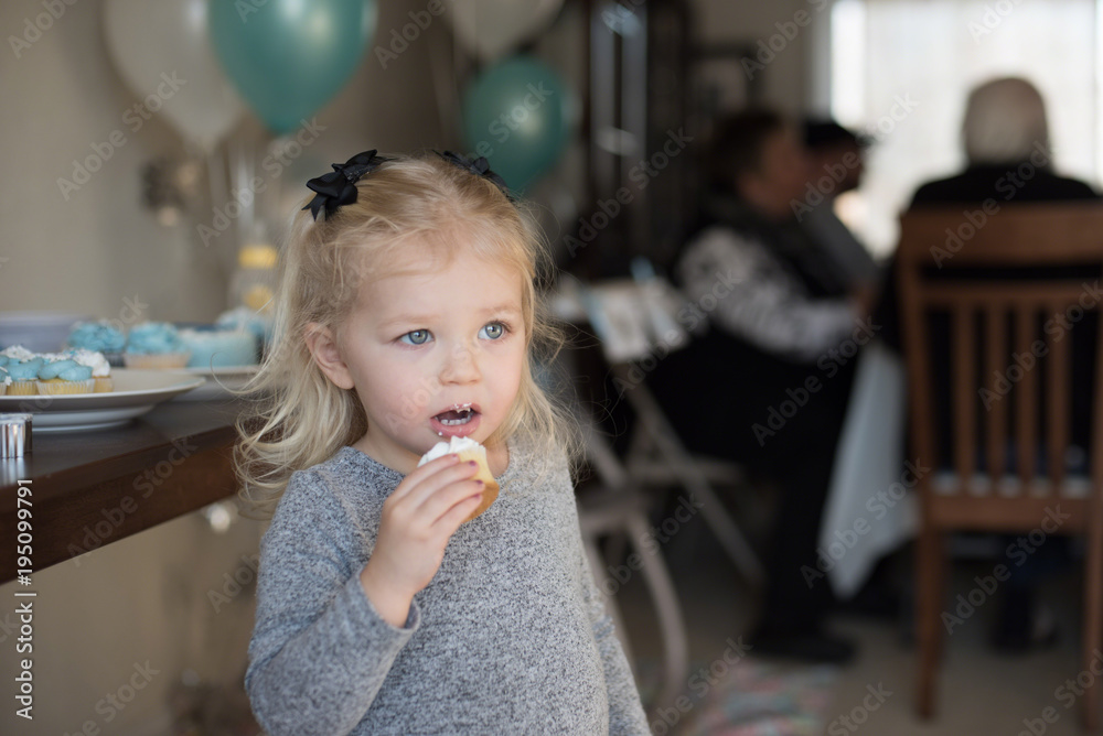 little girl holding a cupcake with icing on face at family birthday party little girl holding a cupcake with icing on face at family birthday party
