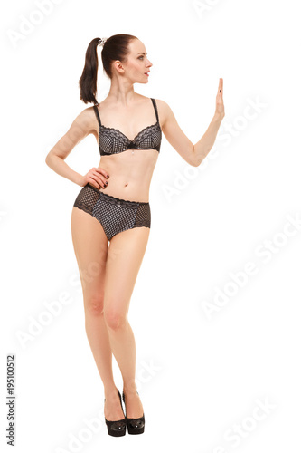 A young woman holds the palm of her left hand at the level of her shoulder. Fashion model in lingerie poses in studio