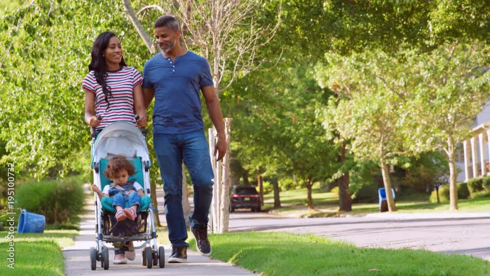 Couple Push Daughter In Stroller As They Walk Along Street