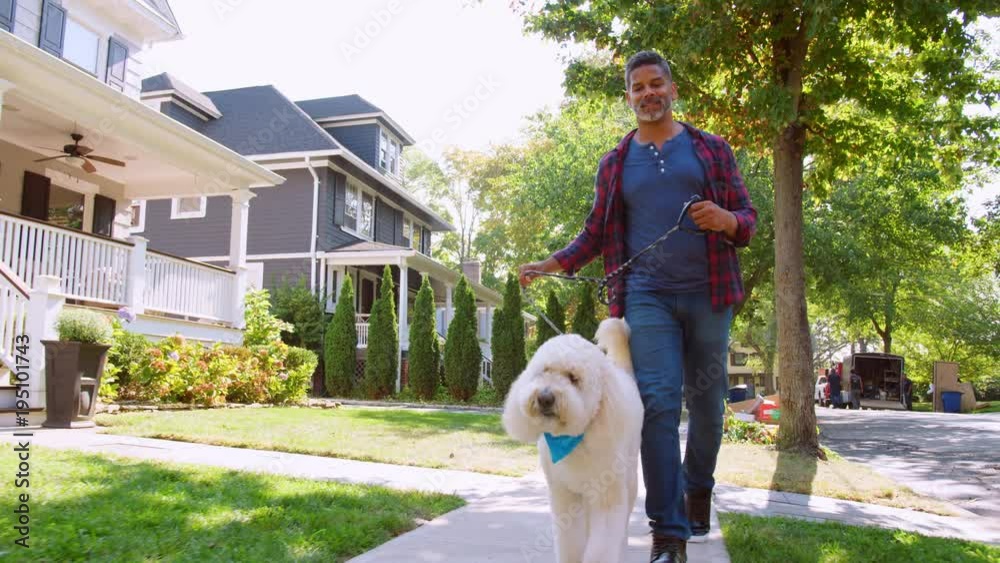 Low Angle Shot Of Man Walking Dog Along Suburban Street
