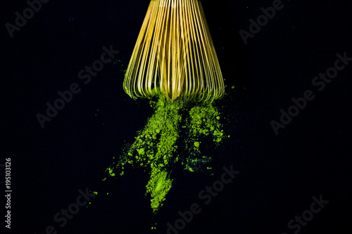 Close up bamboo whisk and matcha green tea powder on black background.