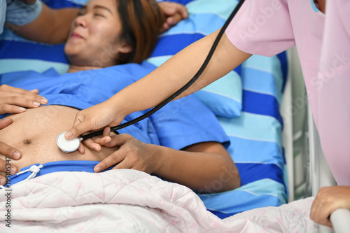 Doctor, nurse examining pregnant woman with stethoscope at maternity ward
