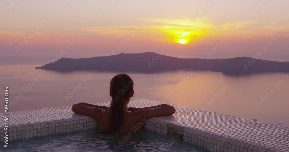 Woman In Swimming Pool Spa Enjoying Sunset On Over Sea Luxury Vacation Travel On Santorini, Greece, Europe. Girl in bikini watching beautiful view of sunset enjoying her holidays at resort hotel.