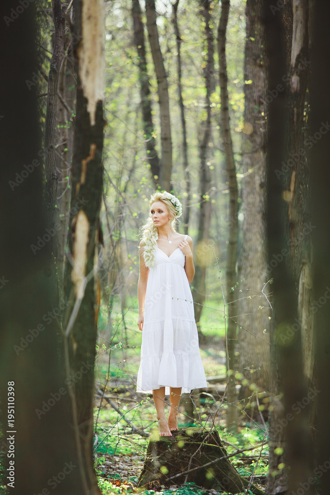 young woman with blond hair in white dress forest among trees.