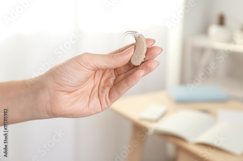 Woman holding hearing aid on blurred background, closeup