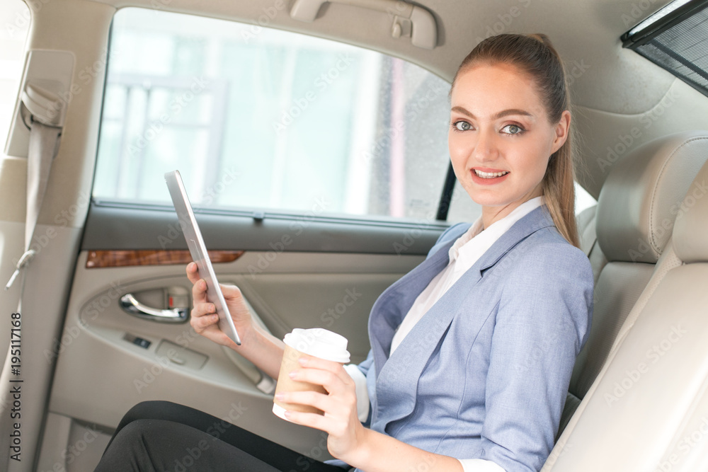 Attractive female using a tablet while sitting in a car to go to work, Woman working overtime concept.