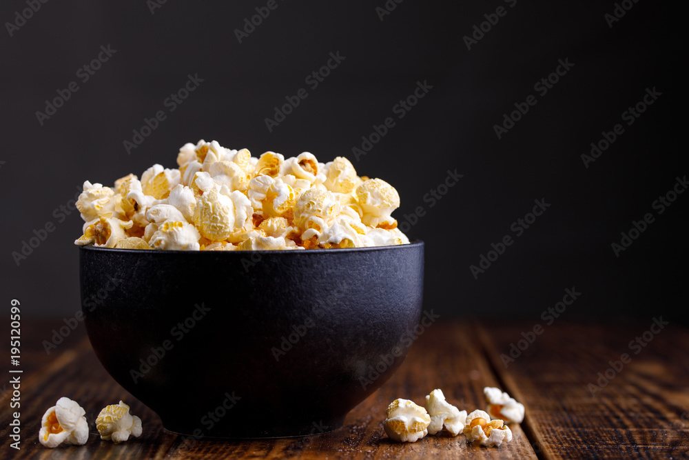 Popcorn in a ceramic bowl and scattered on a wooden background.
