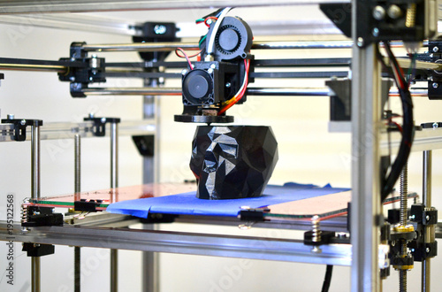 3D printer printing a model in the form of black skull close-up. The 4ht industrial revolution. Automatic three dimensional performs plastic modeling. Progressive modern additive technology photo