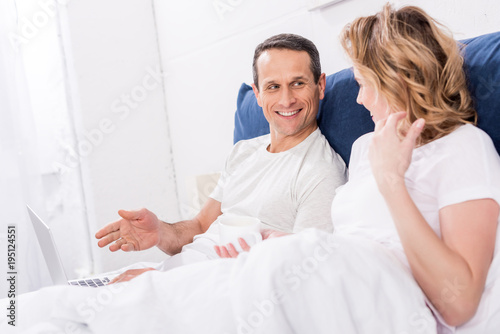 smiling couple with laptop in bed at home