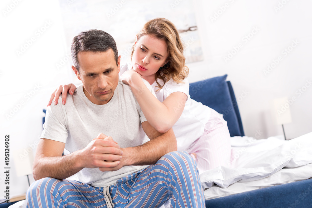 woman hugging sad husband that sitting on bed at home woman hugging sad husband that sitting on bed at home