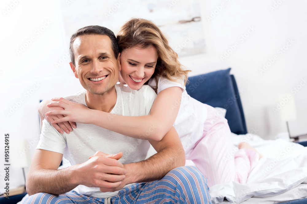portrait of woman hugging smiling husband that sitting on bed at home portrait of woman hugging smiling husband that sitting on bed at home