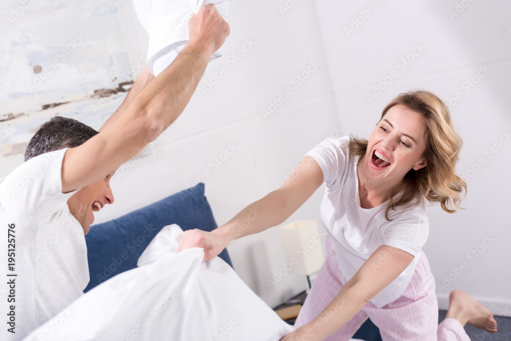 happy couple having pillow fight in bedroom at home happy couple having pillow fight in bedroom at home