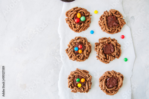 Chocolate bird's nest cookies decorated with colorful candies on a white background. Top view.