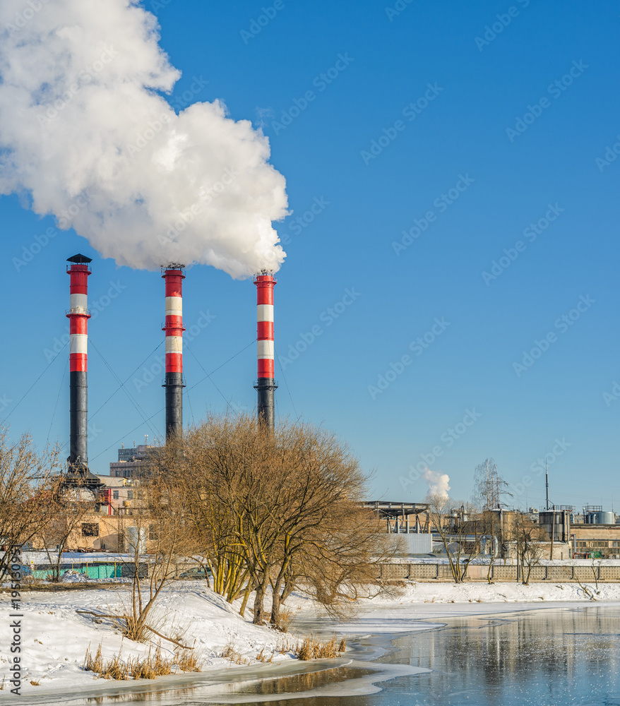 Thermal power plant during winter operation on the river bank. High chimneys emit a large amount of smoke