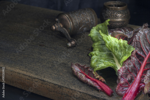 Fresh leaves of swiss chard in green and burgundy colors on a dark wooden background. Vintage style. Free space for text.