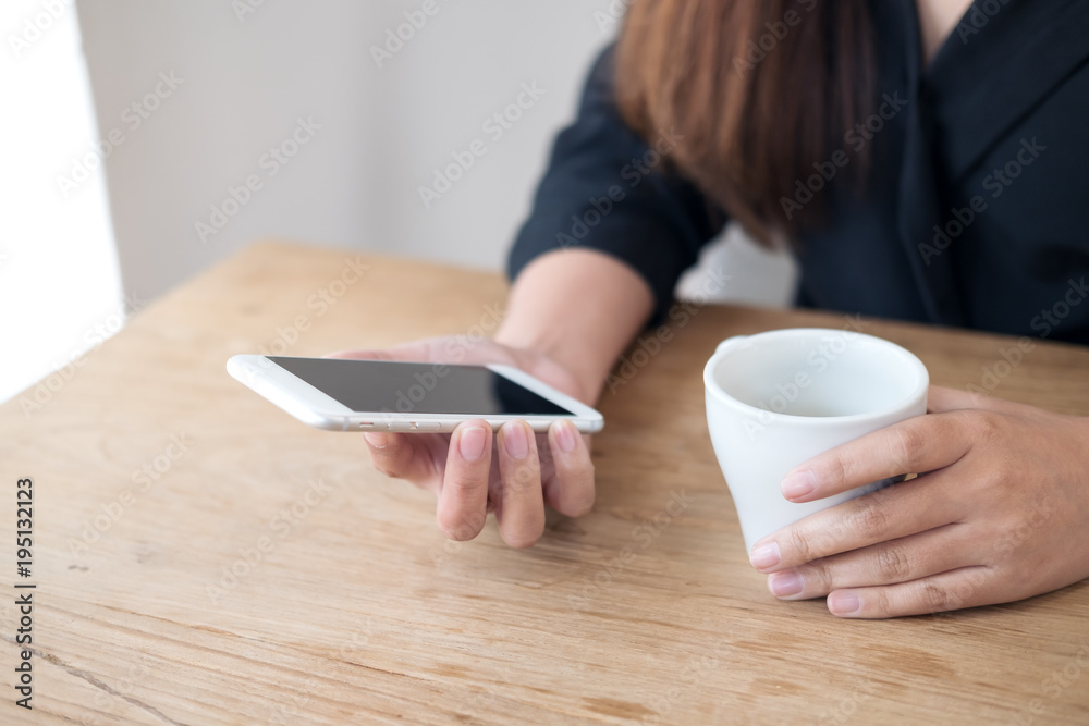 Closeup image of woman's hands holding white mobile phone and coffee cup on wooden table Closeup image of woman's hands holding white mobile phone and coffee cup on wooden table