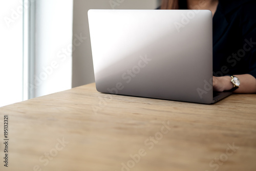 Closeup image of a woman working and typing on laptop on wooden table in office
