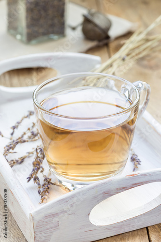 Herbal lavender tea in glass cup with lavender flowers on wooden tray, vertical