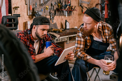 handsome mechanics with tablet drinking beer at garage
