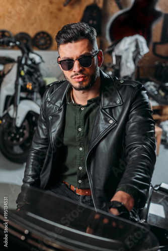 handsome rockabilly man sitting on bike at garage