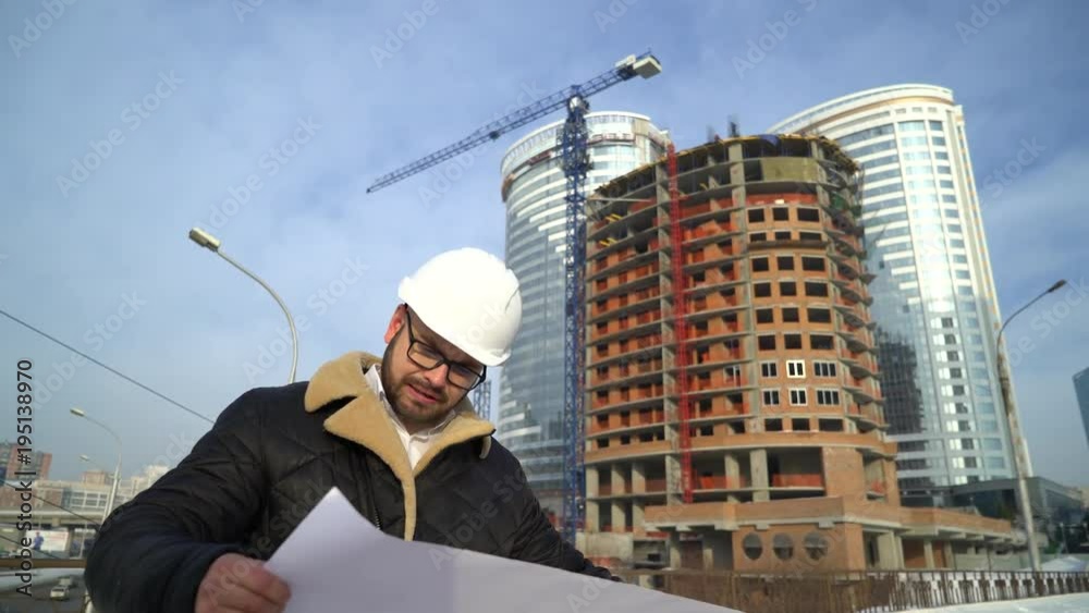 The engineer or the builder checks and controls the object under construction. He goes by the construction site, the workers are working. Against the background of innovative modern buildings. 4 k The engineer or the builder checks and controls the object under construction. He goes by the construction site, the workers are working. Against the background of innovative modern buildings. 4 k