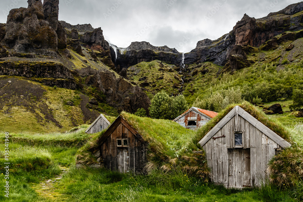 Icelandic turf houses and rocks with waterfall in the background near Kalfafell vilage, Southern Iceland