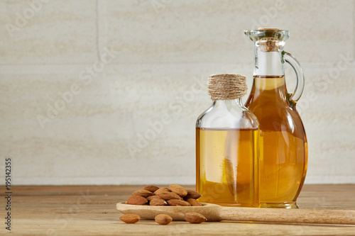 Aromatic oil in a glass jar and bottle with almond in a scoop on wooden table, close-up. photo