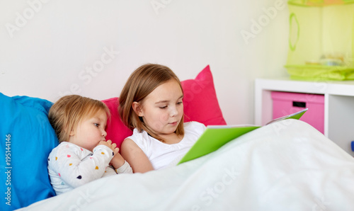 little girls or sisters reading book in bed