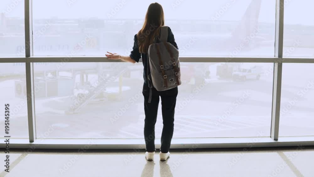 Young woman with backpack near terminal window. Caucasian female tourist using smartphone in airport lounge. Travel. 4K. Young woman with backpack near terminal window. Caucasian female tourist using smartphone in airport lounge. Travel. 4K.