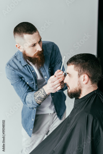 side view of barber cutting customer hair at barbershop isolated on white
