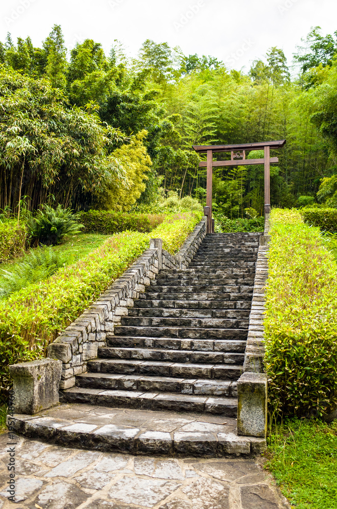 A large stone stairway going up to a wooden japanese torii gate surrounded by tropical vegetation with bamboo.