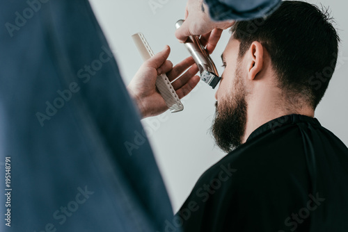 cropped image of barber trimming customer beard at barbershop