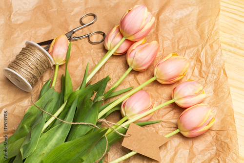Fototapeta Naklejka Na Ścianę i Meble -  Tulipanes rosas junto a una tijera e hilo sisal sobre un fondo de papel marrón arrugado. Vista superior y de cerca.