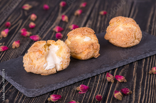 Three tasty cakes of Shue from custard paste with cream stuffing lie on on a plate stone of rectangular on a dark  wooden table. photo