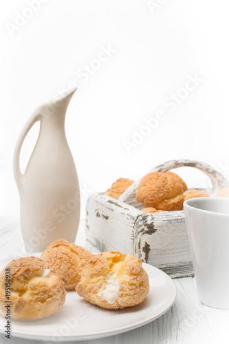 Many tasty cakes of Shue from custard paste with cream stuffing lie on a round plate on a  white wooden table. photo