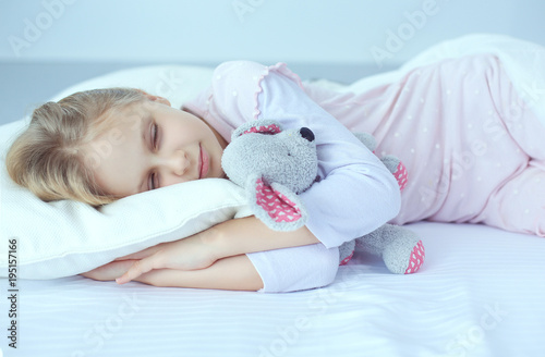 Child little girl sleeps in the bed with a toy teddy bear