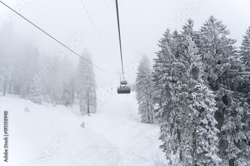 chairlift in a ski resort in the Alps in deep winter with snow covered trees in bad foggy weather