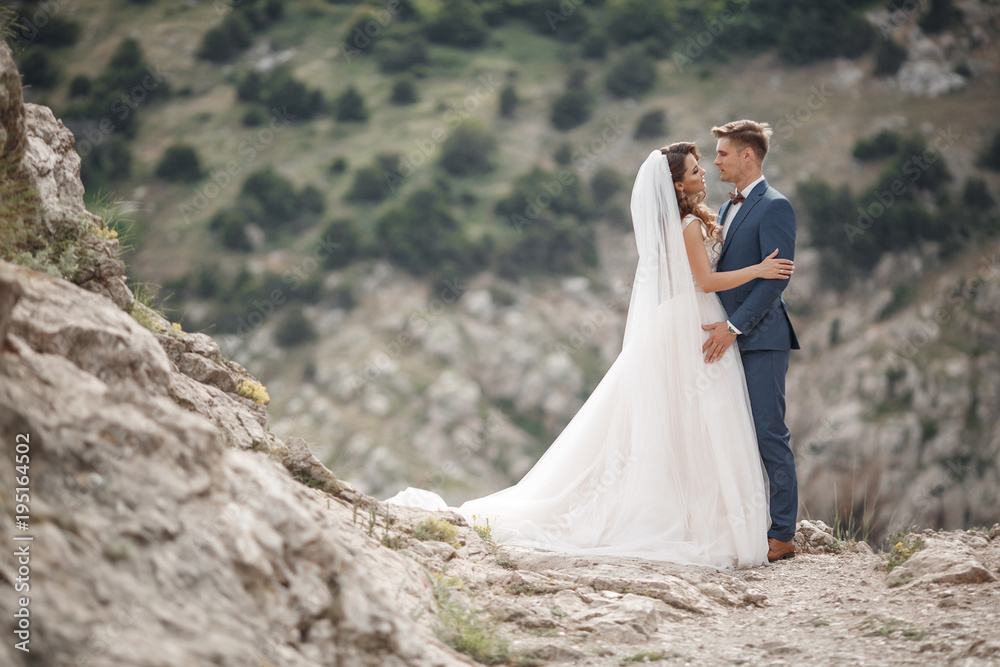 A beautiful bride and groom on their wedding day walk along a rocky shore near the sea.Honeymoon,Happy smiling bride and groom,spending time together in a mountainous area.Happy Wedding Day.