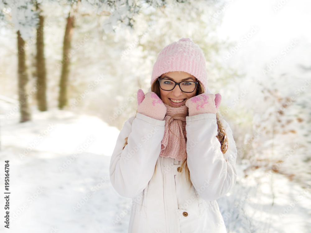 Adorable happy young blonde woman in pink knitted hat scarf having fun strolling snowy winter forest in nature Adorable happy young blonde woman in pink knitted hat scarf having fun strolling snowy winter forest in nature