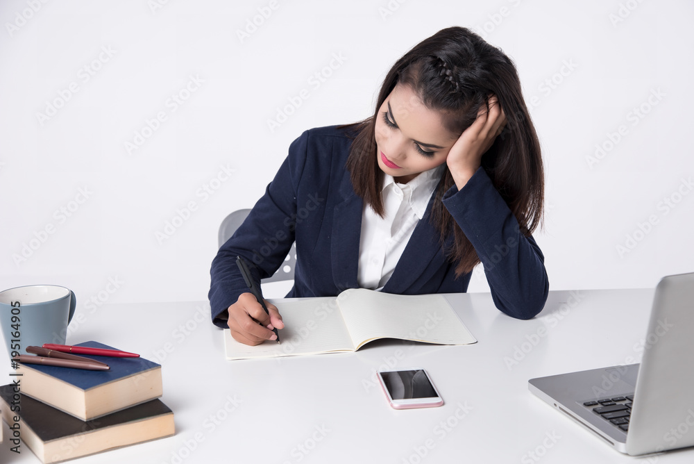 Beautiful office woman sit at table in office ,she work with laptop and look down to book, use pen write report on notebook. She think about her work ,look serious. Beautiful office woman sit at table in office ,she work with laptop and look down to book, use pen write report on notebook. She think about her work ,look serious.