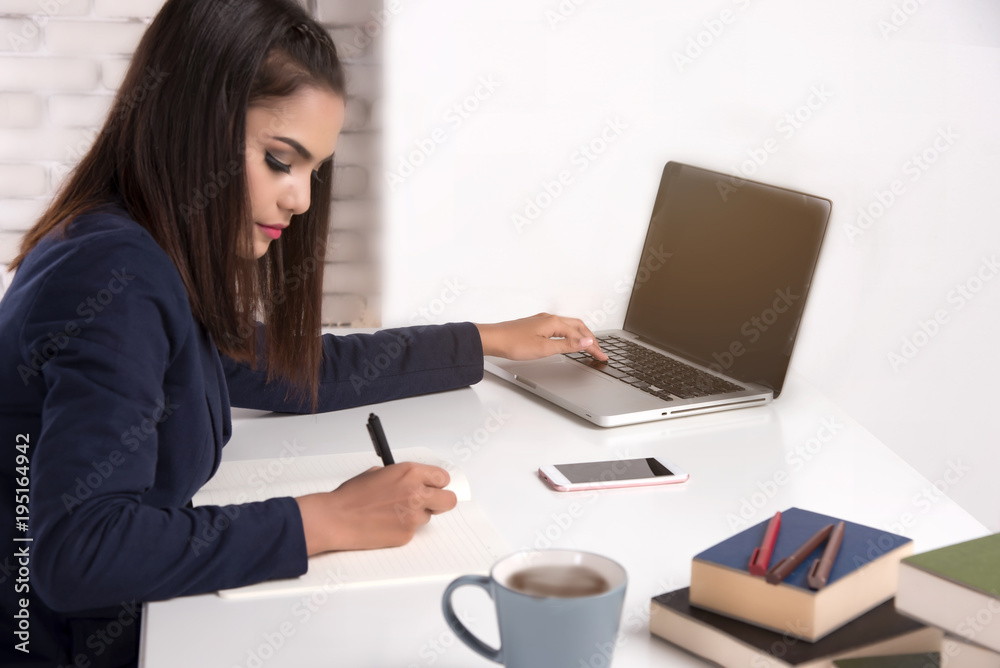 Beautiful office woman sit at table in office ,she work with laptop and use pen write report on notebook. Beautiful office woman sit at table in office ,she work with laptop and use pen write report on notebook.