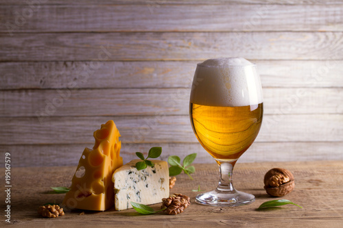 Beer and cheese. Glass of beer with cheese, walnuts and basil on wooden background. Ale and food concept
