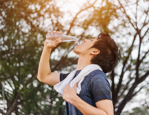 young sporty man drinking water in park