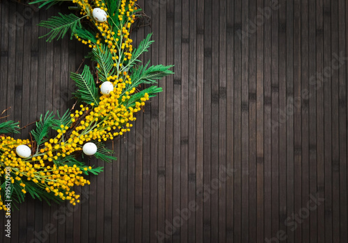 Wreath of mimosa with eggs on a brown background