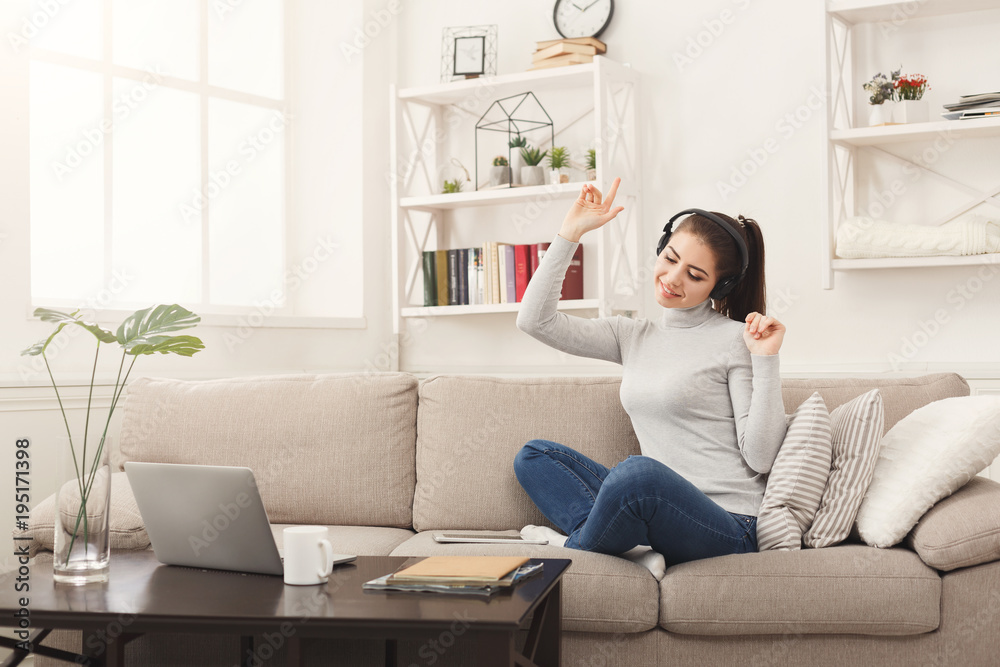 Happy young woman in headphones on beige couch Happy young woman in headphones on beige couch