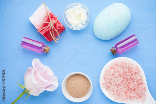 Spa and natural cosmetics concept. Set of sea salt, rose, natural clay ,shea oil, glass bottles and other spa treatment tools on the blue wooden background. Top view. Space for a text. Close up.